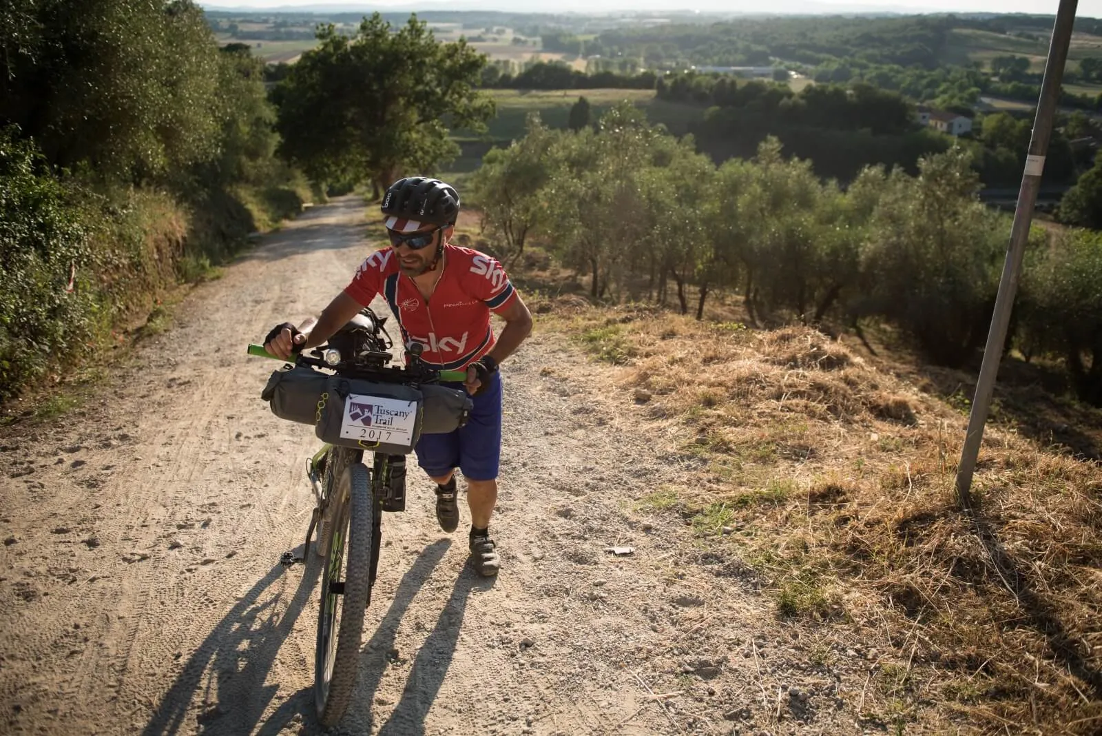 Un rider spinge la bici in salita su una strada bianca