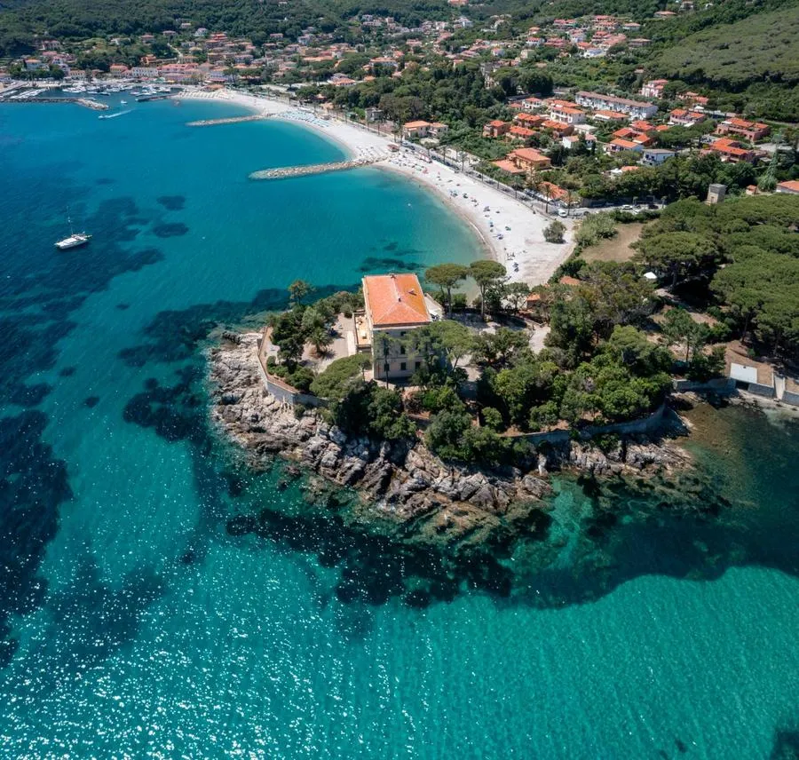 Baia dell'Isola d'Elba con la spiaggia, il paese dietro e una villa sul promontorio