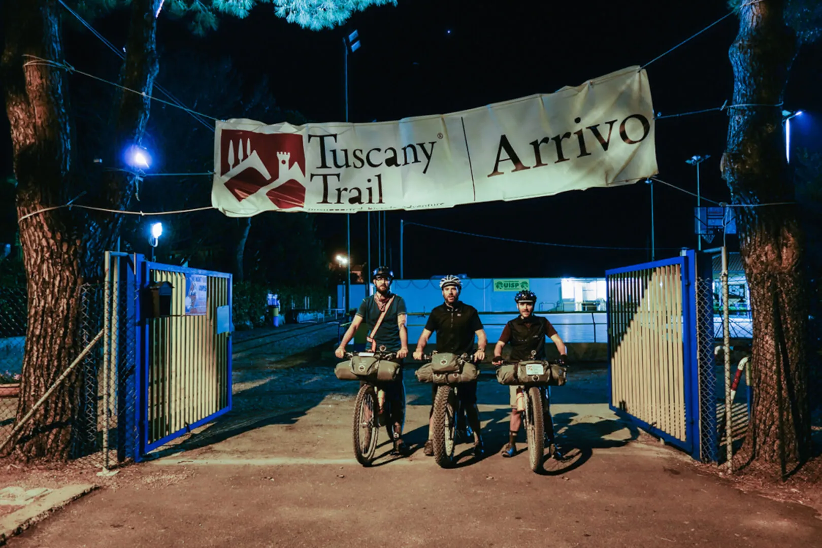 Tre ciclisti sotto l'arco d'arrivo del Tuscany Trail, di notte