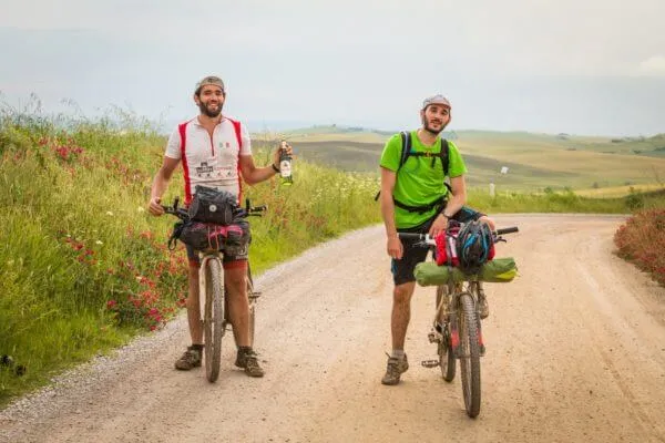 Due rider su una strada bianca alzano le braccia